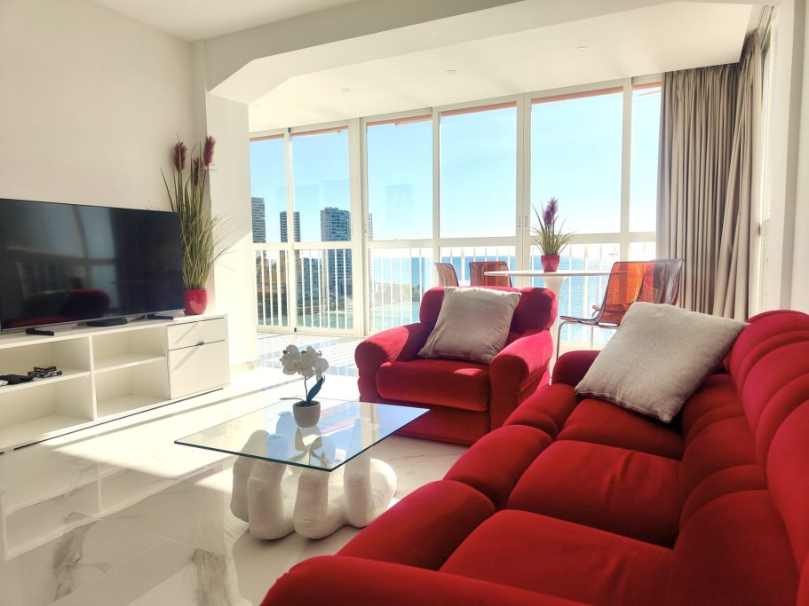 Salon confortable Salon design avec canapé rouge et baie vitrée vue mer – appartement Veracruz Collection Signature Benidorm