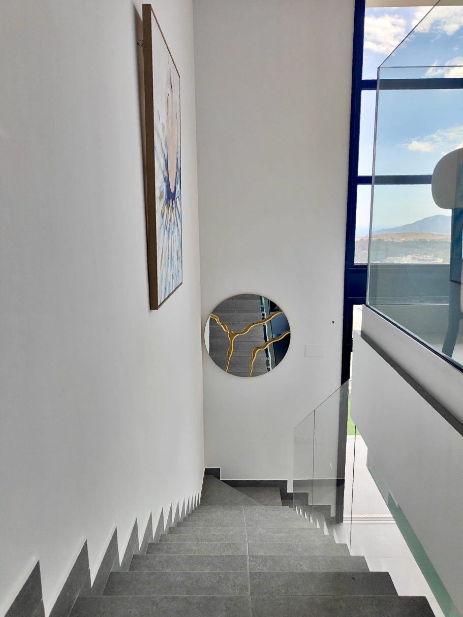 Hall d’entrée avec escalier gris moderne, garde-corps en verre et miroir design – villa Collection Signature Polop Hills