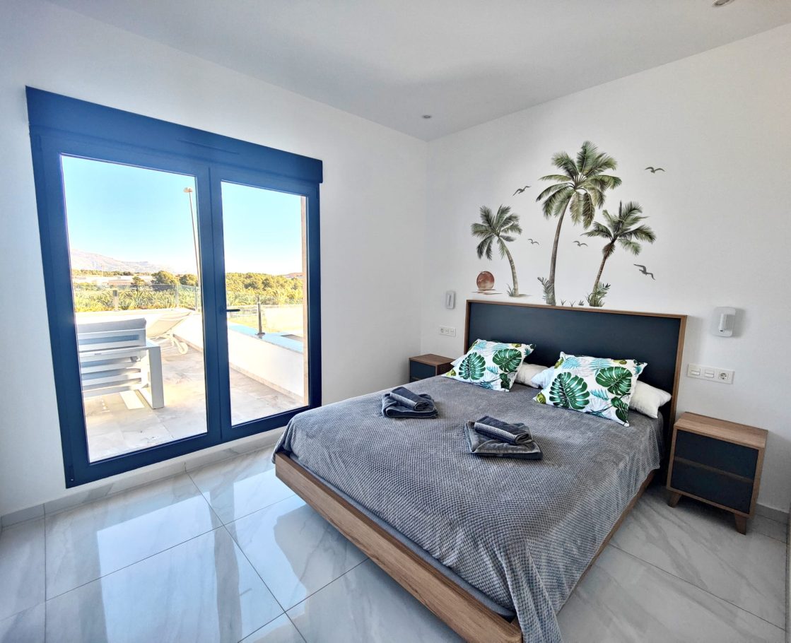 Chambre double avec décoration palmier et baie vitrée sur terrasse – villa Don Benito Altos de Polop